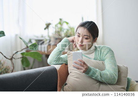 Woman relaxing on sofa and looking at smartphone 114140036