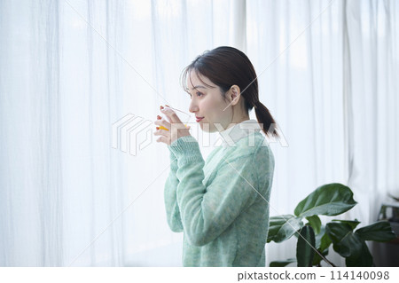 一名20多歲的女子在窗邊喝著柳橙汁 114140098
