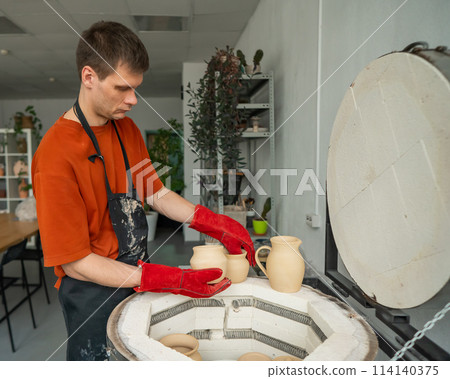 Caucasian man loading ceramic products into a special kiln. Caucasian man loading ceramic products into a special kiln. 114140375