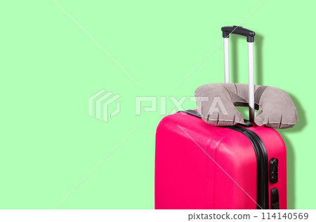 Pink suitcase and gray travel pillow on a green background. 114140569
