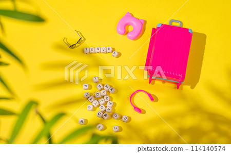Flat lay pink toy suitcase with travel accessories on a yellow background with shadow. 114140574