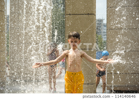 Boy meditating in water fountain find ZEN. Child playing with a city fountain on hot summer day. Happy kids having fun in fountain. Summer weather. Active leisure, lifestyle and vacation 114140646