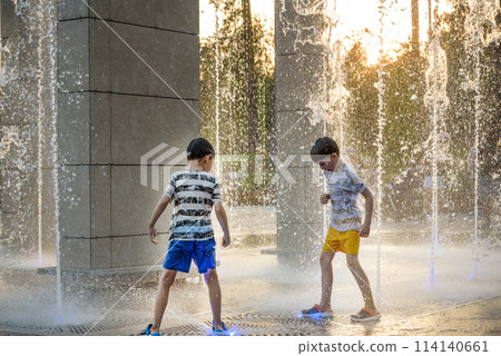 Boys jumping in water fountains. Children playing with a city fountain on hot summer day. Happy friends having fun in fountain. Summer weather. Friendship, lifestyle and vacation 114140661