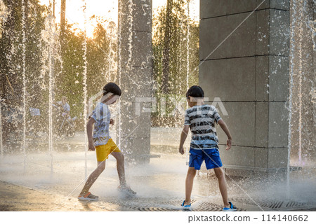 Boys jumping in water fountains. Children playing with a city fo 114140662