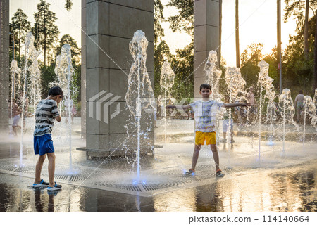 Boys jumping in water fountains. Children playing with a city fountain on hot summer day. Happy friends having fun in fountain. Summer weather. Friendship, lifestyle and vacation 114140664