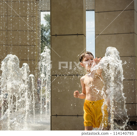 Boy having fun in water fountains. Child playing with a city fountain on hot summer day. Happy kids having fun in fountain. Summer weather. Active leisure, lifestyle and vacation 114140793