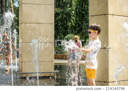 Boy having fun in water fountains. Child playing with a city fountain on hot summer day. Happy kids having fun in fountain. Summer weather. Active leisure, lifestyle and vacation Boy having fun in water fountains. Child playing with a city fountain on hot summer day. Happy kids having fun in fountain. Summer weather. Active leisure, lifestyle and vacation 114140796