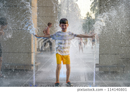 Boy having fun in water fountains. Child playing with a city fountain on hot summer day. Happy kids having fun in fountain. Summer weather. Active leisure, lifestyle and vacation 114140801