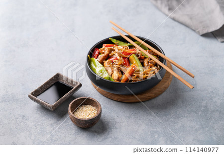 Stir-fry with soba noodles, meat and vegetables on a light background with chopsticks, soy sauce Stir-fry with soba noodles, meat and vegetables on a light background with chopsticks, soy sauce 114140977
