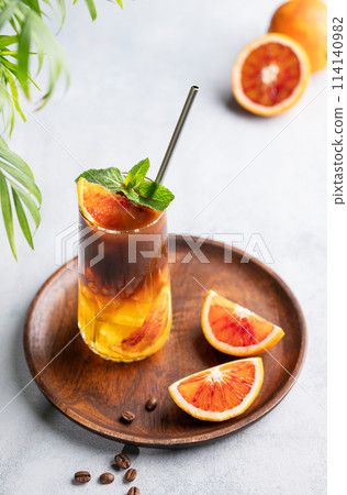 Coffee with orange juice (bumble) in a tall glass with ice and mint on a wooden plate Coffee with orange juice (bumble) in a tall glass with ice and mint on a wooden plate 114140982