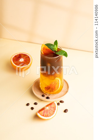 Americano coffee with orange juice (bumble) in a tall glass with ice and mint on a yellow background Americano coffee with orange juice (bumble) in a tall glass with ice and mint on a yellow background 114140986