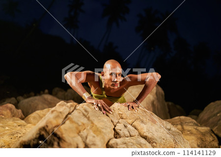 Gender fluid black person crawling like wild primeval animal on rock in creek natural water pool at night. Queer ethnic fashion model in long revealing clothes moves creepily in the middle of lake. Gender fluid black person crawling like wild primeval animal on rock in creek natural water pool at night. Queer ethnic fashion model in long revealing clothes moves creepily in the middle of lake. 114141129
