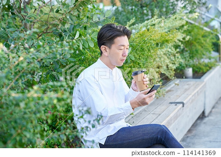 A man drinking coffee and using a smartphone A man drinking coffee and using a smartphone 114141369