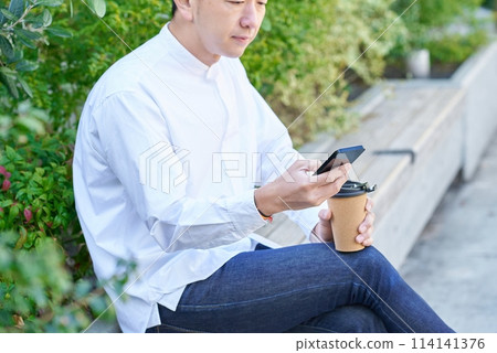 一名男子一邊喝咖啡一邊操作智慧型手機 一名男子一邊喝咖啡一邊操作智慧型手機 114141376