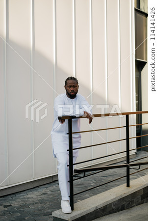 Cheerful male tourist dress in white wear dashiki ethnic smiling at city street on stairs. African American travel model have free time. Copy space 114141426
