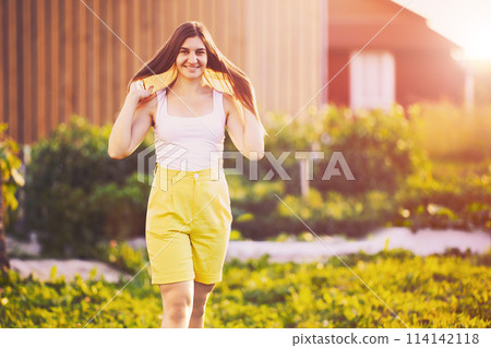 Portrait of European woman in her 20s wearing Bermuda shorts on summer evening in countryside. Portrait of European woman in her 20s wearing Bermuda shorts on summer evening in countryside. 114142118