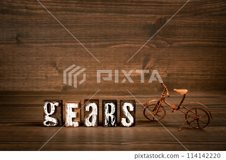 GEARS. Text from alphabet blocks and rusty miniature bicycle on wood texture background GEARS. Text from alphabet blocks and rusty miniature bicycle on wood texture background 114142220