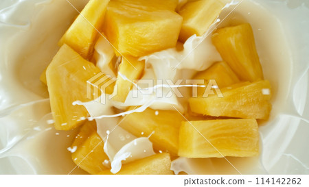 Fresh pineapple pieces falling into yoghurt cream, top down view 114142262