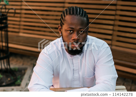 Close up portrait of a happy african american man smiling wearing ethnic dashiki clothes outdoor in summer cafe terrace background. Millennial generation student and youth. Close up portrait of a happy african american man smiling wearing ethnic dashiki clothes outdoor in summer cafe terrace background. Millennial generation student and youth. 114142278