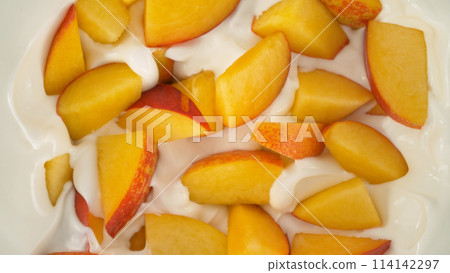 Fresh nectarines pieces falling into yoghurt cream, top down view 114142297