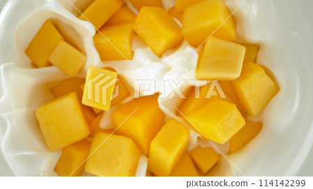 Fresh mango pieces falling into yoghurt cream, top down view 114142299