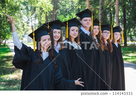 Row of happy young people in graduation gowns outdoors. Students in the park. Row of happy young people in graduation gowns outdoors. Students in the park. 114143331
