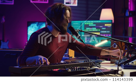 Skilled musician composing a song on piano midi controller, working with mixing console and daw software to record music. Artist singing at microphone, mastering his acoustical notes. Camera A. Skilled musician composing a song on piano midi controller, working with mixing console and daw software to record music. Artist singing at microphone, mastering his acoustical notes. Camera A. 114143399