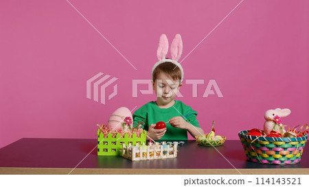 Smiling jolly preschooler painting eggs and ornaments for easter festivity preparations, using art and craft materials to decorate festive arrangements. Young boy having fun with tie dye. Camera B. 114143521