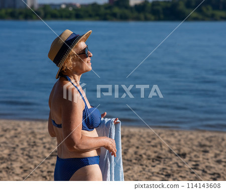 An old woman in a straw hat, sunglasses and a swimsuit is resting on the beach. An old woman in a straw hat, sunglasses and a swimsuit is resting on the beach. 114143608