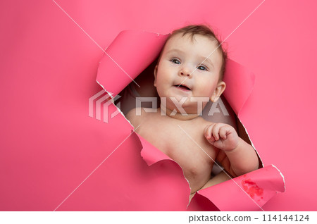 Cute Caucasian newborn baby boy peeks out of a hole in a paper pink background. Cute Caucasian newborn baby boy peeks out of a hole in a paper pink background. 114144124