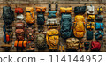 A collection of backpacks and other gear are laid out on a wooden surface. The backpacks come in a variety of colors and sizes, and the gear includes items such as a tent, sleeping bags 114144952