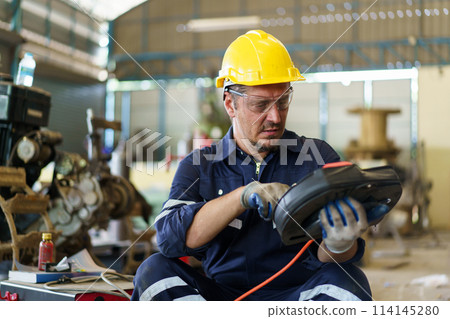 Professional caucasian white ethnicity male technician operating the heavy duty machine in the lathing factory. Technician in safety and helmet suit controlling a machine in factory. Professional caucasian white ethnicity male technician operating the heavy duty machine in the lathing factory. Technician in safety and helmet suit controlling a machine in factory. 114145280