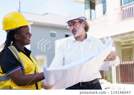 Team of engineer discuss at construction site. Female black ethnicity engineer taking to caucasian white client about the construction plan in blue print. Team of engineer discuss at construction site. Female black ethnicity engineer taking to caucasian white client about the construction plan in blue print. 114146047