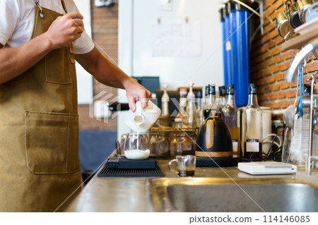 Professional Asian male barista pouring a cold milk in a glass. Happy male barista making a cup of iced latte coffee in a small coffee shop. Small business concept. 114146085