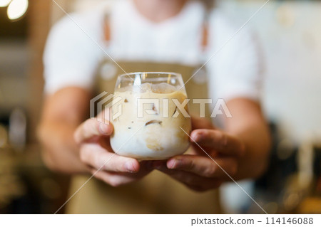 Professional Asian male barista pouring a cold milk in a glass. Happy male barista making a cup of iced latte coffee in a small coffee shop. Small business concept. Professional Asian male barista pouring a cold milk in a glass. Happy male barista making a cup of iced latte coffee in a small coffee shop. Small business concept. 114146088