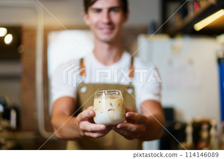 Professional Asian male barista pouring a cold milk in a glass. Happy male barista making a cup of iced latte coffee in a small coffee shop. Small business concept. Professional Asian male barista pouring a cold milk in a glass. Happy male barista making a cup of iced latte coffee in a small coffee shop. Small business concept. 114146089
