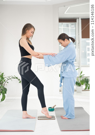 Caucasian woman stands on sadhu boards with therapist support. 114146186