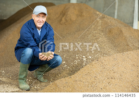Portrait of mature man farmer holding handful of calf feed in animal feed warehouse 114146435