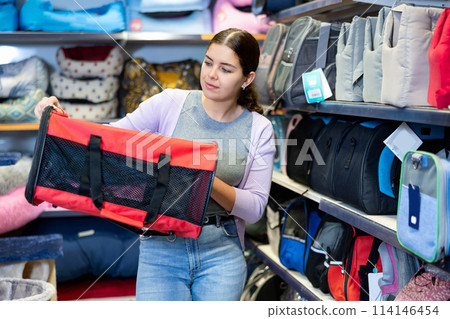 Young woman choosing fabric pet carrier bag for cats in pet shop Young woman choosing fabric pet carrier bag for cats in pet shop 114146454