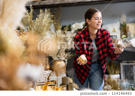 Cheerful young woman woman choosing between two candlesticks in a Christmas shop Cheerful young woman woman choosing between two candlesticks in a Christmas shop 114146493