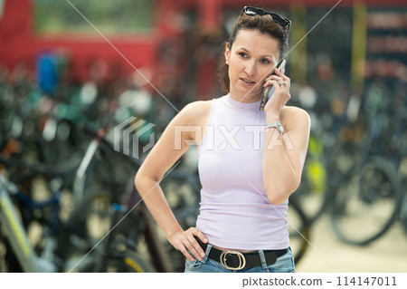 Woman making phone call while shopping in bicycle store 114147011