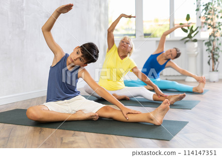 Preteen boy practicing revolved head to knee pose of yoga in light fitness room 114147351