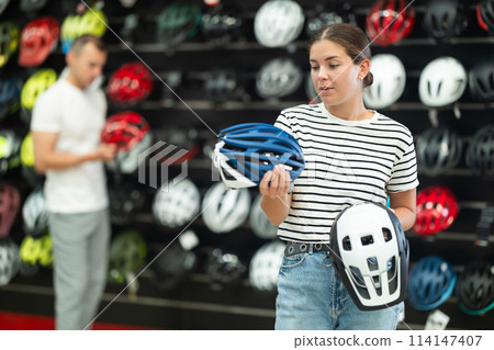 Young girl comparing two bicycle helmets in specialized shop 114147407