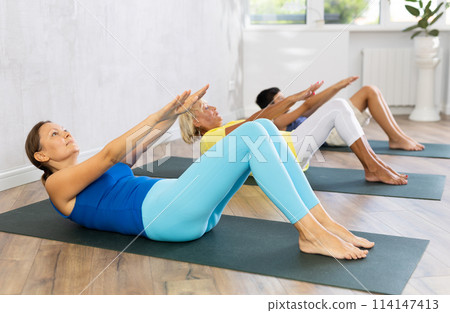 Middle-aged woman practicing yoga pose lying on back on black rug 114147413