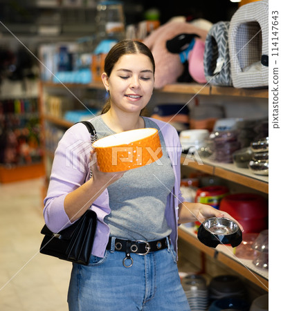 Young happy woman choosing bowl for pets in pet shop Young happy woman choosing bowl for pets in pet shop 114147643