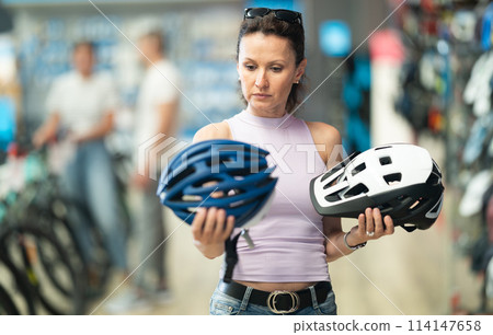 Adult woman choosing bicycle helmet in store 114147658
