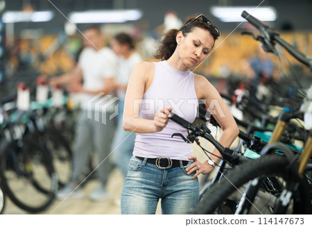 Female shopper inspecting bicycle handlebars and controls in store 114147673