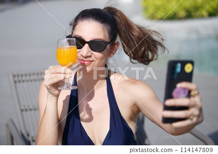 woman wearing a bikini and sunglasses using smartphone camera take photo selfie woman wearing a bikini and sunglasses using smartphone camera take photo selfie 114147809