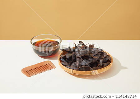 Brown background against some ingredients of locust's product, a rattan tray contains some black locust pods, a glass bowl of locust extract and wooden comb. Space for text and displaying product Brown background against some ingredients of locust's product, a rattan tray contains some black locust pods, a glass bowl of locust extract and wooden comb. Space for text and displaying product 114148714