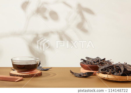 Locust fruits featured on rattan tray and wooden dish on the right side and a transparent bowl with brown liquid inside placed on the left of photo. Front view, blank space Locust fruits featured on rattan tray and wooden dish on the right side and a transparent bowl with brown liquid inside placed on the left of photo. Front view, blank space 114148722